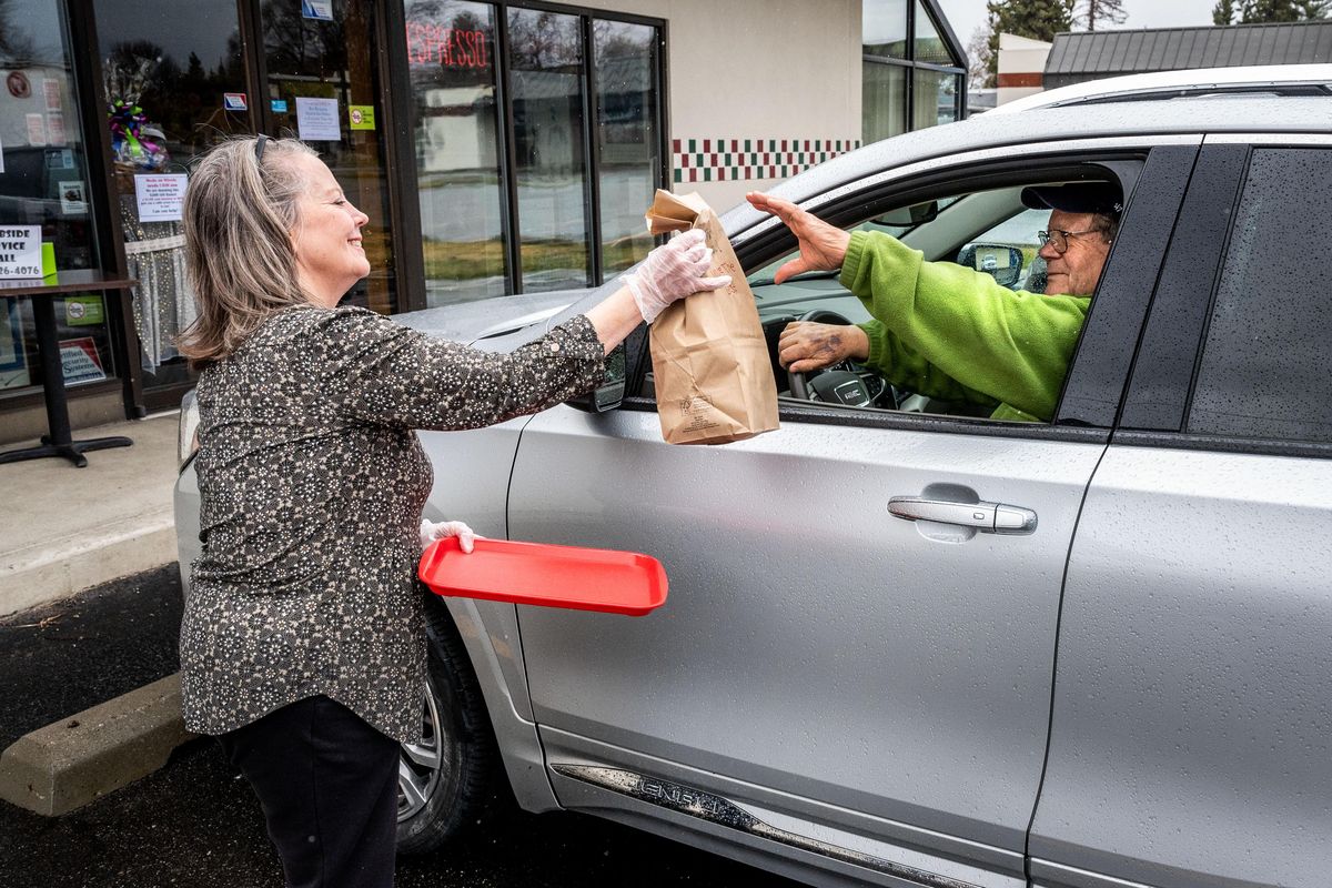 Cindy Hallett, owner of Halletts Market & Cafe in Spokane Valley, hands Gil Cook a food order. Besides curbside orders and pickup, the market is also open with social distancing measures, such as plexiglass around the cash register and a hand sanitizer station just inside the front door. (Colin Mulvany / The Spokesman-Review)