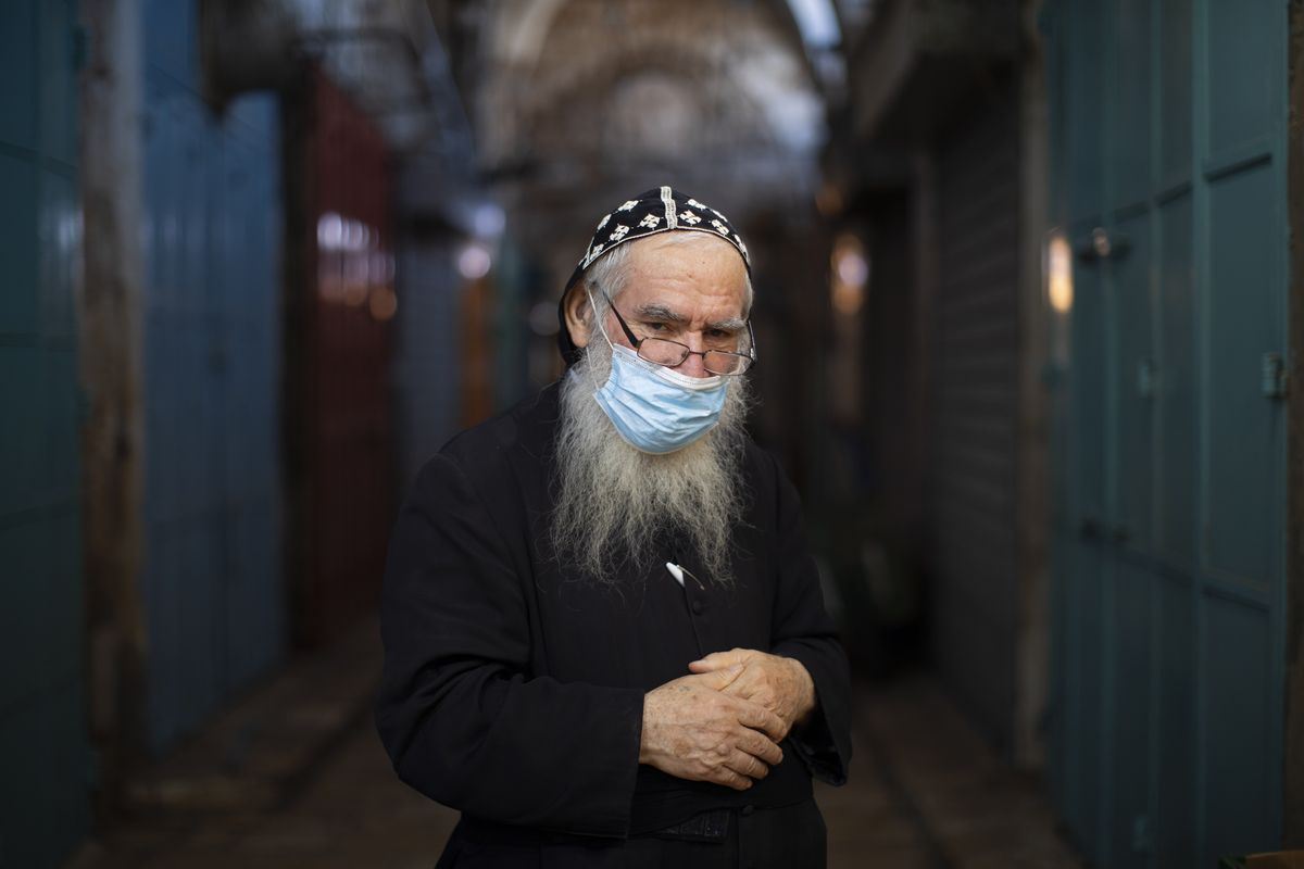 Syrian Orthodox priest Shimon Jan, 70, poses for a portrait wearing his protective face mask Tuesday in the alleys of Jerusalem’s Old City.  (Oded Balilty)