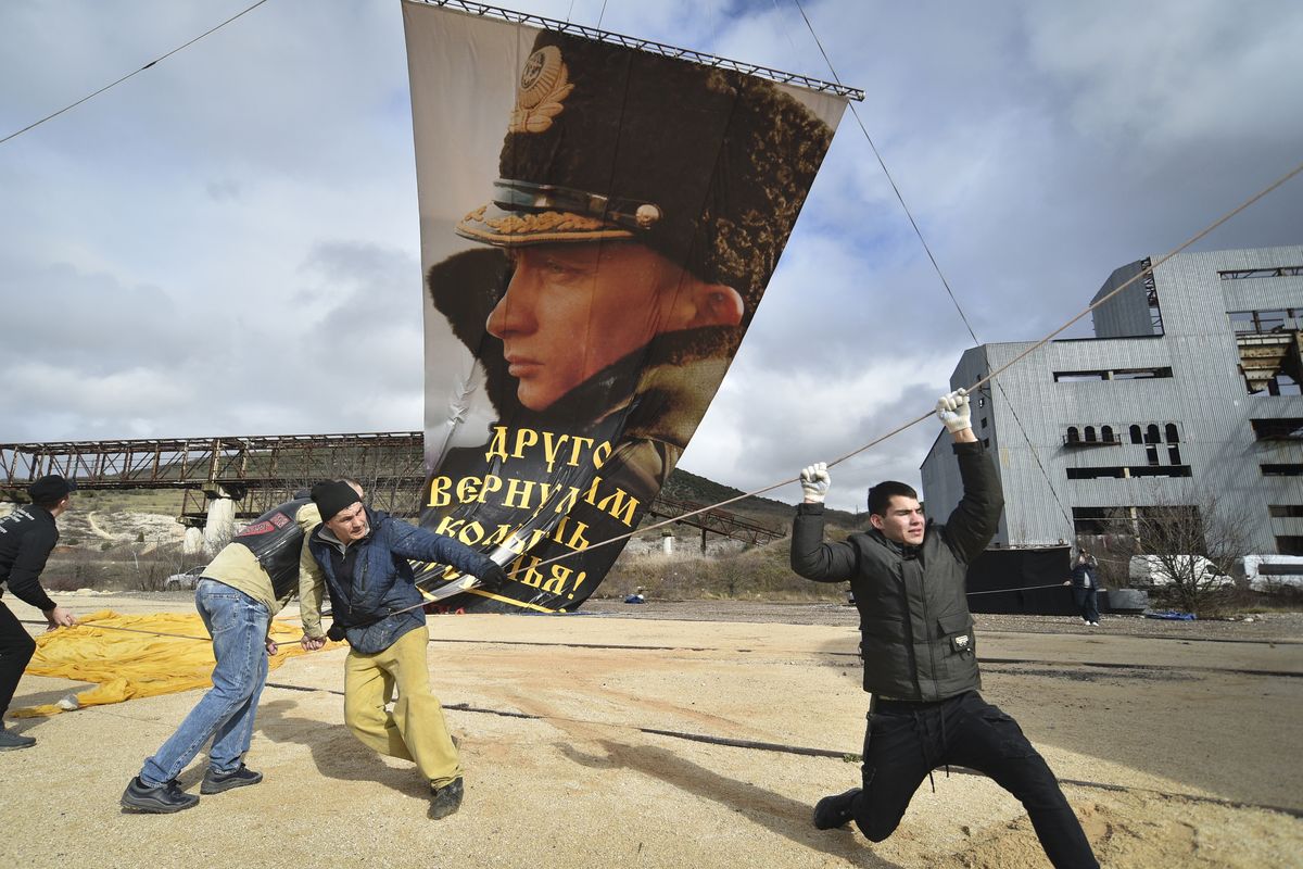 Enthusiasts fix a portrait of Russian President Vladimir Putin to a balloon during celebration of the anniversary of Crimea annexation from Ukraine in 2014, in Sevastopol, Crimea, Thursday, March 18, 2021. Residents of cities in Crimea and Russia are holding gatherings to commemorate the seventh anniversary of Russia