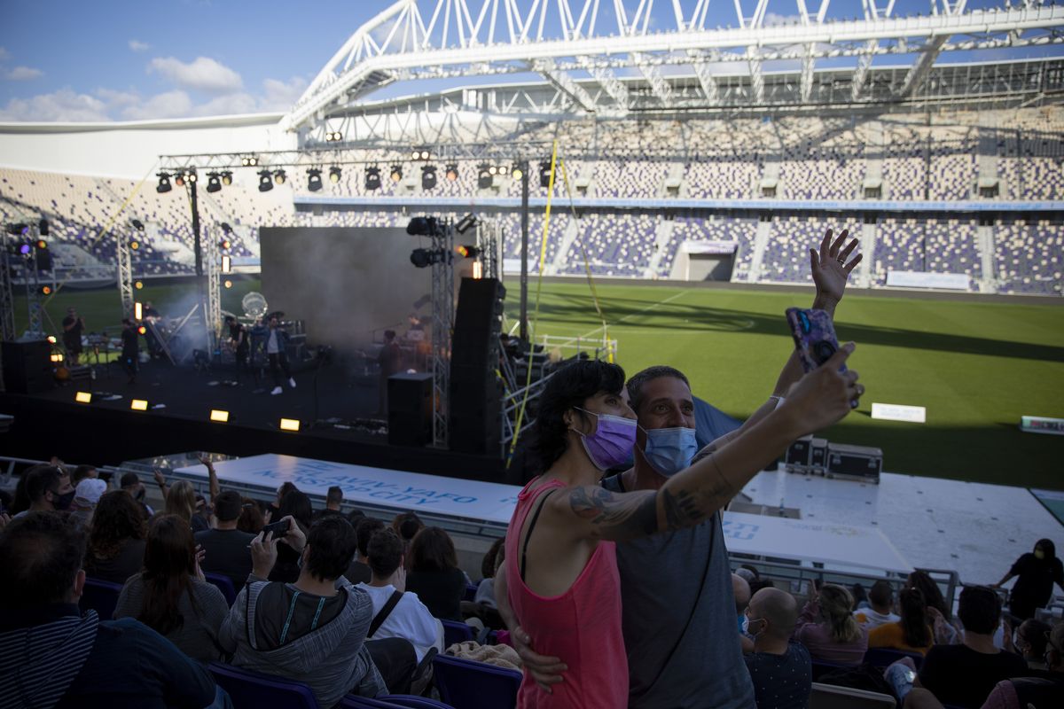 Audience members wearing protective face masks take a selfie during a performance of Israeli musician Ivri Lider, where all guests were required to show "green passport" proof of receiving a COVID-19 vaccination or full recovery from the virus at a soccer stadium in Tel Aviv, Friday, March. 5, 2021. (Oded Balilty)
