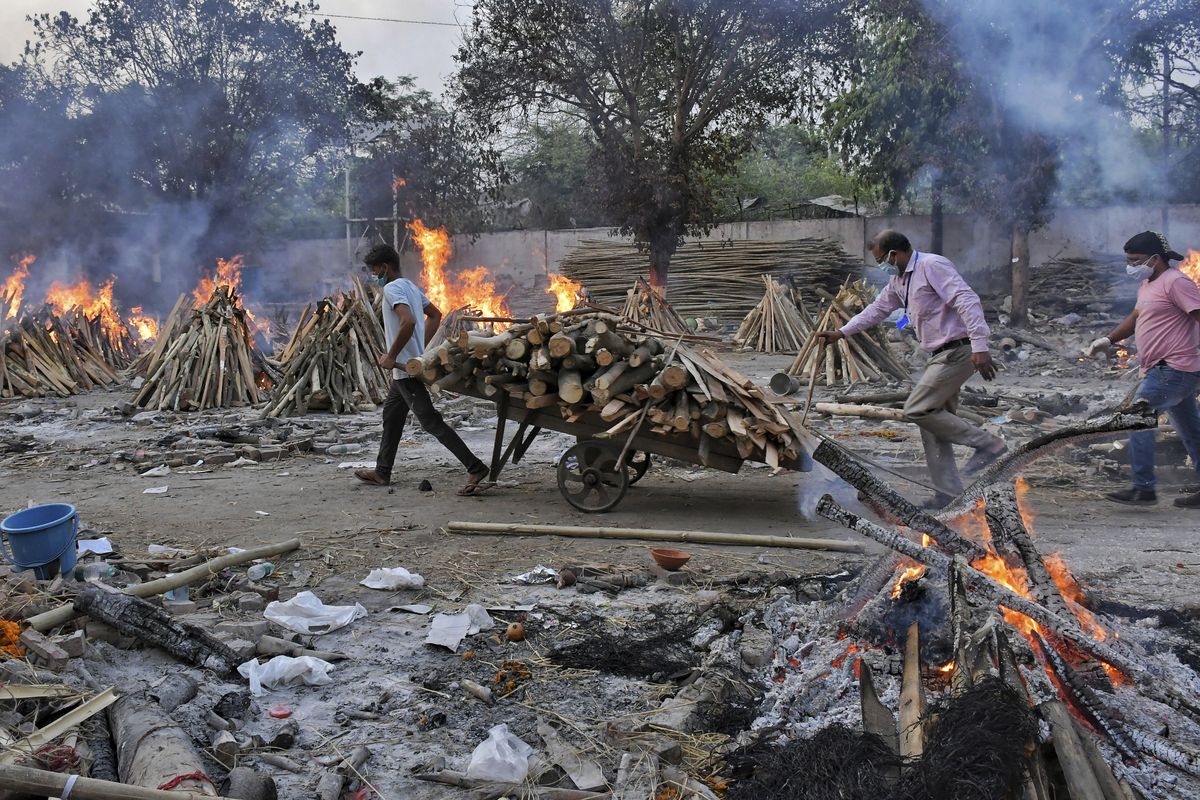 A worker carries wood on a hand cart as multiple funeral pyres of COVID-19 victims burn at a crematorium Saturday on the outskirts of New Delhi, India.  (Ishant Chauhan)