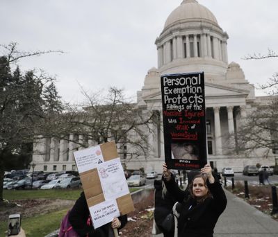 A woman holds a sign opposing a proposed bill that would remove parents’ ability to claim a philosophical exemption to opt their school-age children out of the combined measles, mumps and rubella vaccine as she stands near the Legislative Building, Friday, Feb. 8, 2019, following a public hearing before the House Health Care & Wellness Committee at the Capitol in Olympia, Wash. (Ted S. Warren / AP)