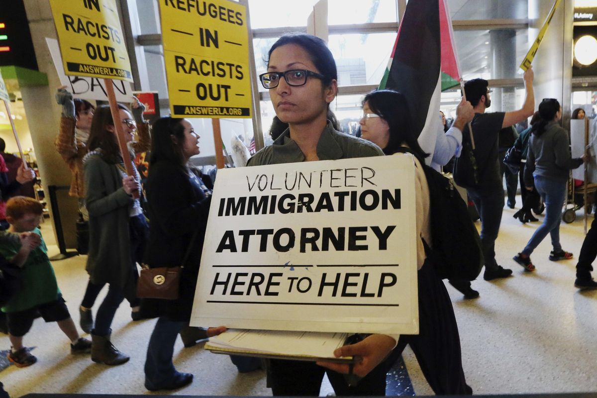 A woman offers legal services at the customs arrival area as demonstrators opposed to President Donald Trump’s executive orders barring entry to the U.S. by Muslims from certain countries march behind at the Tom Bradley International Terminal at Los Angeles International Airport on Saturday, Feb. 4, 2017. (Reed Saxon / Associated Press)