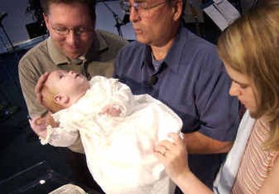 
From left to right, Rob Lemmon, Pastor Gary Hebden and Sarah Lemmon hold Lucas Lemmon during the baby's dedication ceremony at Valley Open Bible Church on Sunday in Spokane Valley. The baptismal gown has been used by four generations of the Storebo family, which keeps a list of the names of the people who have been baptized or dedicated in the gown. Dating back to 1902, the delicate antique linen gown was brought from Norway. 
 (Liz Kishimoto / The Spokesman-Review)
