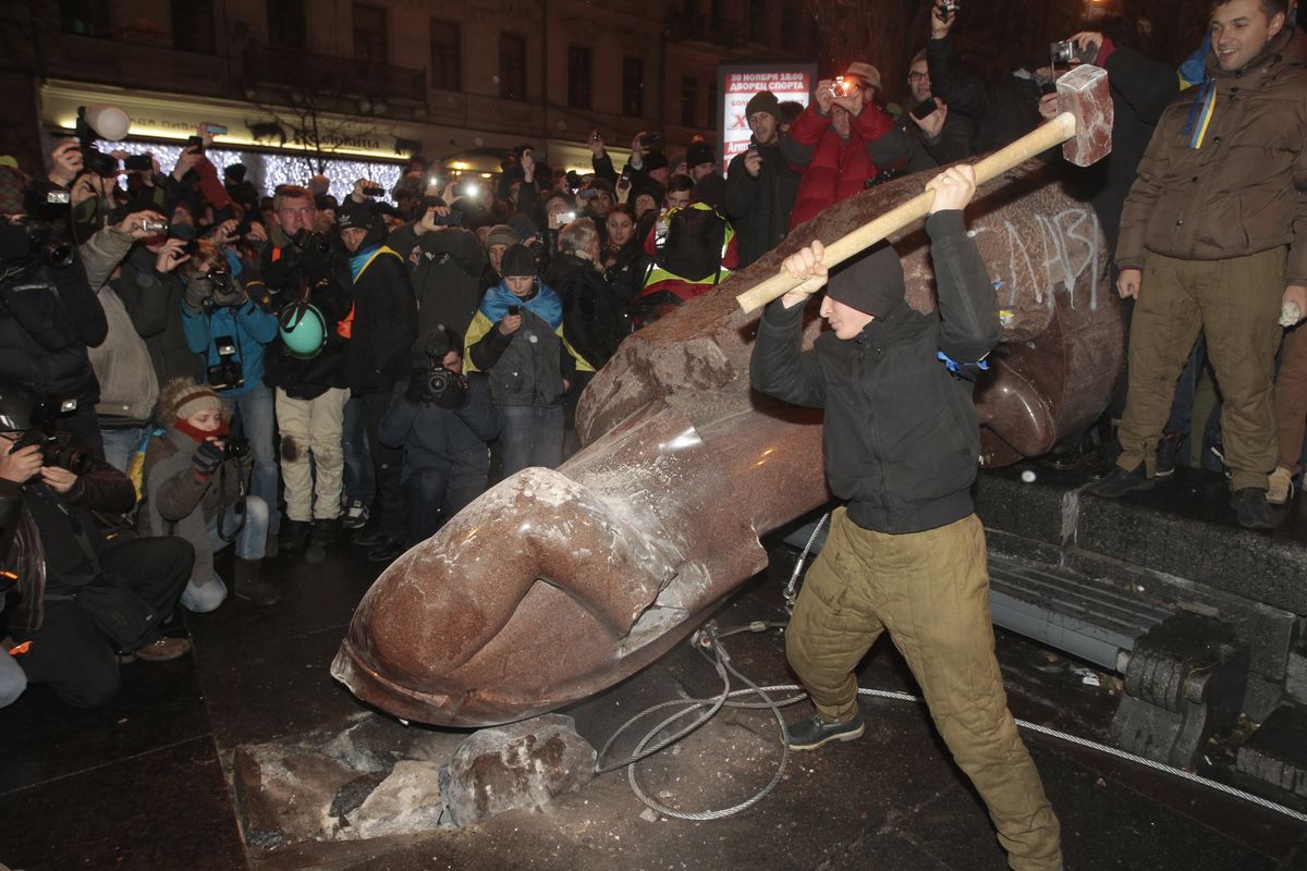 A protester beats the statue of Vladimir Lenin with a sledgehammer in Kiev, Ukraine, on Sunday amid unrest over a trade agreement with Russia. (Associated Press)
