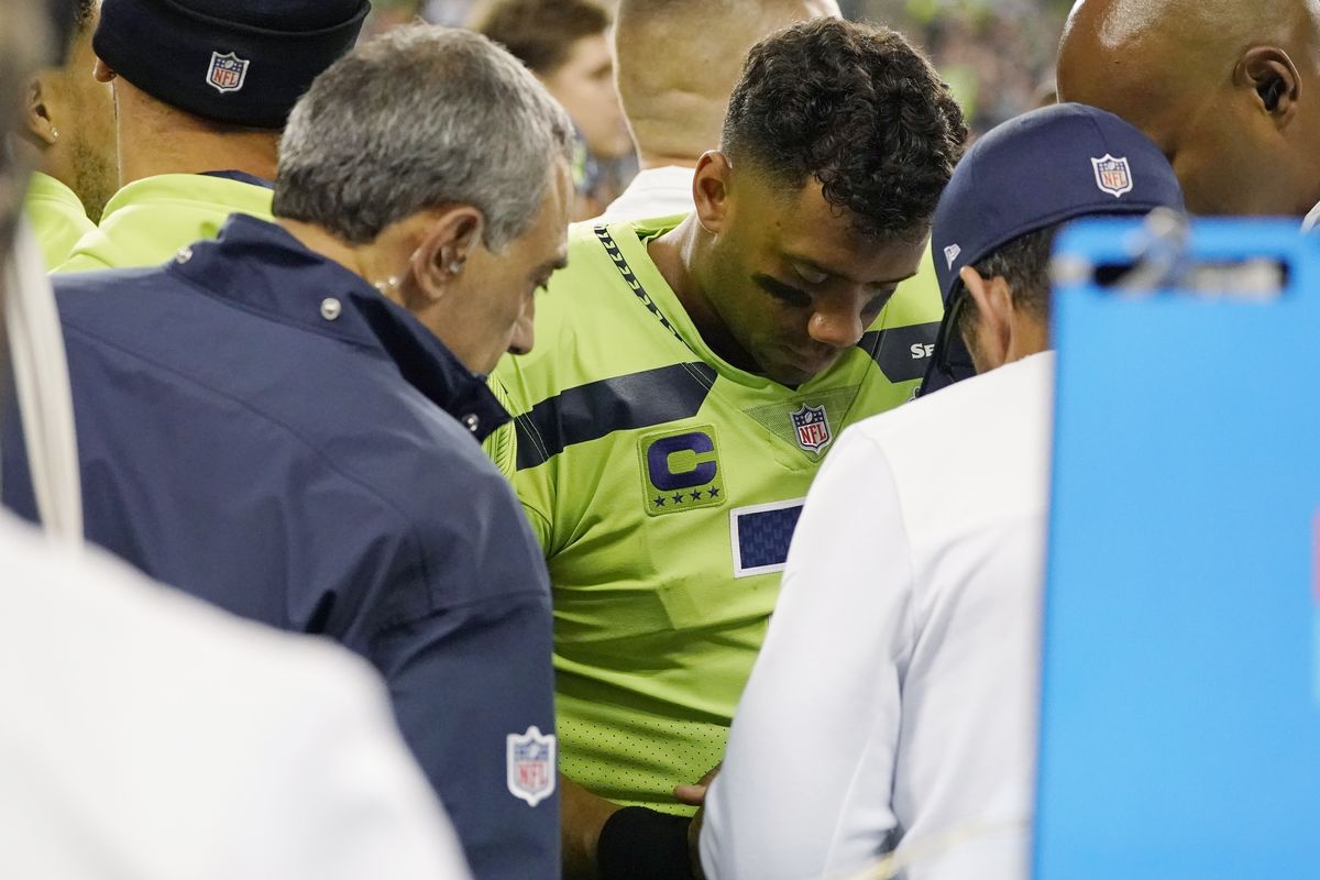 Seattle Seahawks quarterback Russell Wilson has his throwing hand examined on the sideline during the second half of a game against the Los Angeles Rams Thursday in Seattle. Wilson underwent surgery on the injured finger and is expected to be out at least a month.  (Associated Press)