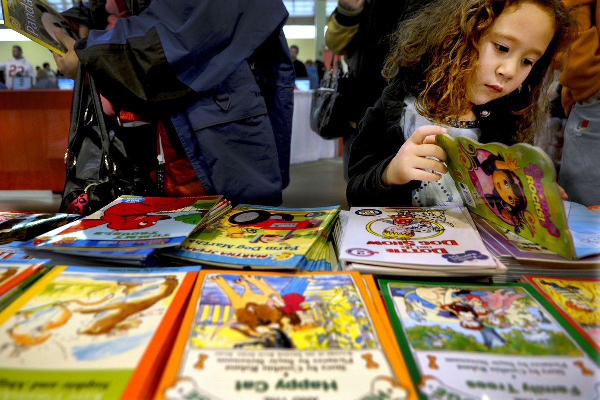 Four-year-old Alxis Marcille chooses a Dora the Explorer book while in line with her mother, Sone Marcillen, at the Christmas Bureau in Spokane on Thursday. The book tables were stocked with a variety of books for children of different ethnicities. (Kathy Plonka)