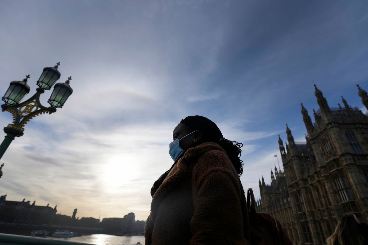 A woman wears a face covering as she crosses Westminster Bridge in London, Thursday, Dec. 9, 2021. British Prime Minister Boris Johnson has announced tighter restrictions to stem the spread of the omicron variant. He is again urging people to work from home and mandating COVID-19 passes to get into nightclubs and large events.  (Frank Augstein)