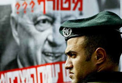 
An Israeli police officer stands guard while a resident, not seen in photo, holds a poster against Prime Minister Ariel Sharon outside Gaza on Sunday. The protester complained that Israel doesn't protect them from militant attacks. 
 (Associated Press / The Spokesman-Review)