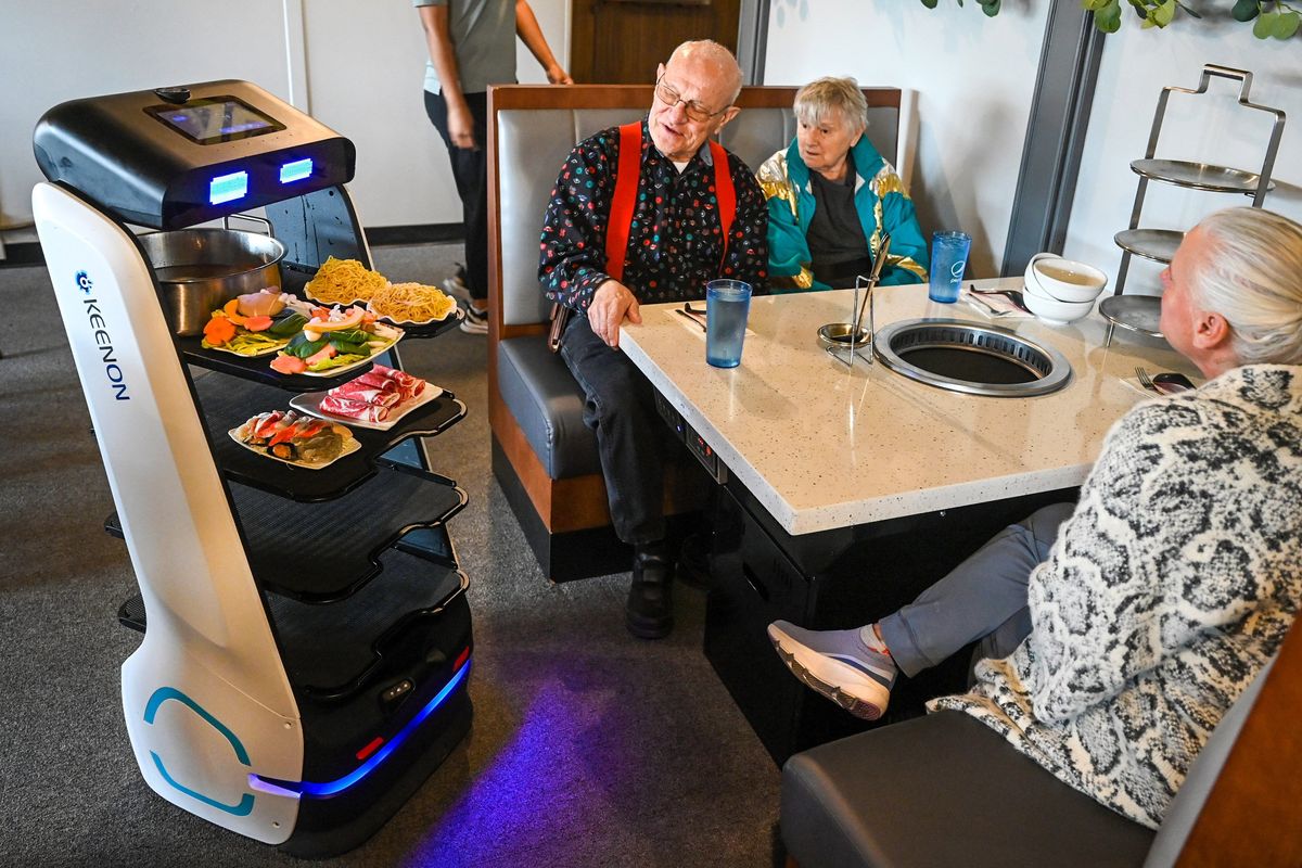 Hot Pot and Pho guests, Jim and Marsha Baumer and their daughter, Becky Baumer, right, watch as pots of broth and ingredients are delivered to their table via a robot that is programmed to wheel its way throughout the restaurant. The raw ingredients are cooked in large pots of boiling broth at a guest