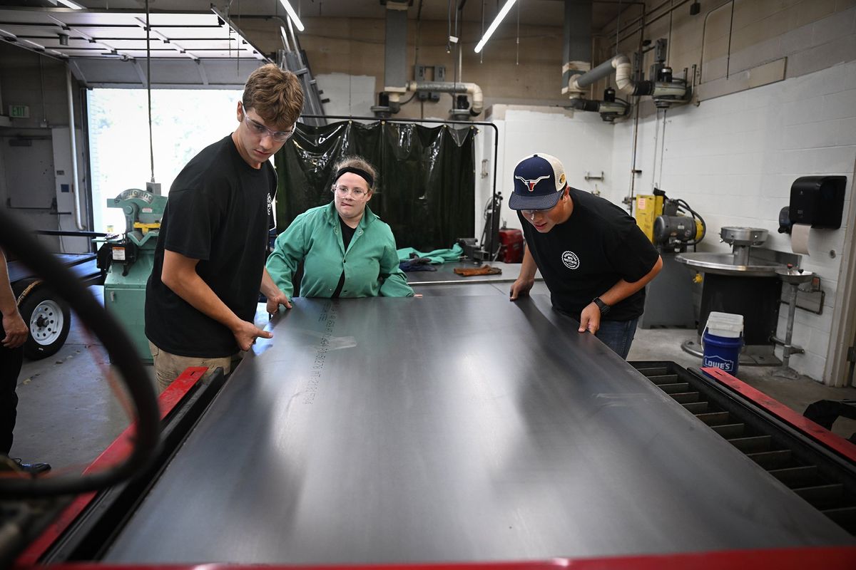 High school students, from left, Wilson Hash, Alexandria Schaffer and Nick McLaughlin load a sheet of steel into the CNC plasma cutter inside the metal shop at East Valley High School Friday, July 14, 2023. They spending two weeks at the Production Manufacturing Institute, a two-week camp for students looking for experience designing and producing products for market. The steel pieces being cut out are intended to manufacture fire pits for sale.  (Jesse Tinsley/The Spokesman-Review)
