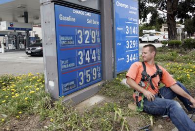 An electrician working on an in-ground power line takes a peek at the  gas prices at a Chevron dealership last week in South San Francisco, Calif.   (Associated Press / The Spokesman-Review)