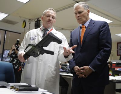 Washington Gov. Jay Inslee, right, talks with Rick Wyant, left, supervisor of the forensic firearms unit at the Washington State Patrol crime laboratory in Seattle, on Jan. 11 as Wyant holds a semi-automatic rifle that has been fitted with a 