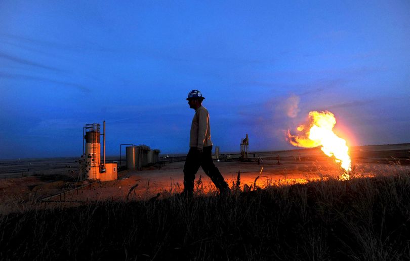 A natural gas flare illuminates an oil well at dusk in March in Williston, N.D., as Coeur d’Alene resident Kevin McLeod walks by. McLeod, who moved to Williston in search of employment, works for B&G Roustabout as a laborer. The oil boom has created thousands of jobs for those willing to relocate to the fields of North Dakota.