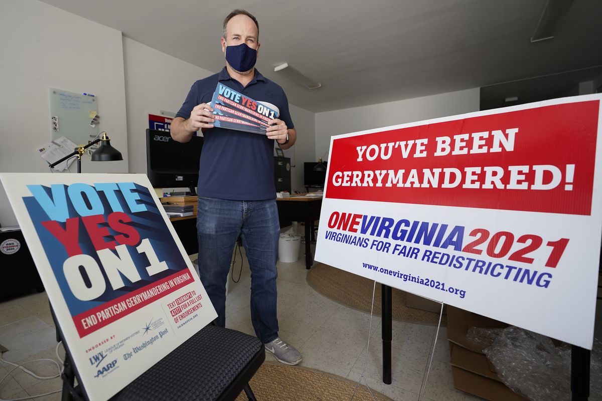 In this Oct. 6, 2020 photo, redistricting reform advocate Brian Cannon poses with some of his yard signs and bumper stickers in his office in Richmond, Va. A new voter-approved commission in Ohio that was supposed to reduce partisanship in the once-a-decade process of political map-drawing has already become a flop. Similar commissions meeting for the first time in New York and Virginia have devolved into partisan finger-pointing, undermining their intent.  (Steve Helber)
