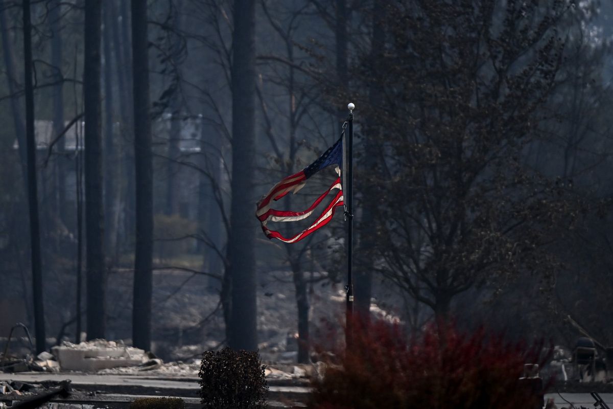 A charred American flag flies over a neighborhood burned by the Old Trails fire on North Pine Place on Monday in Spokane. (Tyler Tjomsland/The Spokesman-Review)