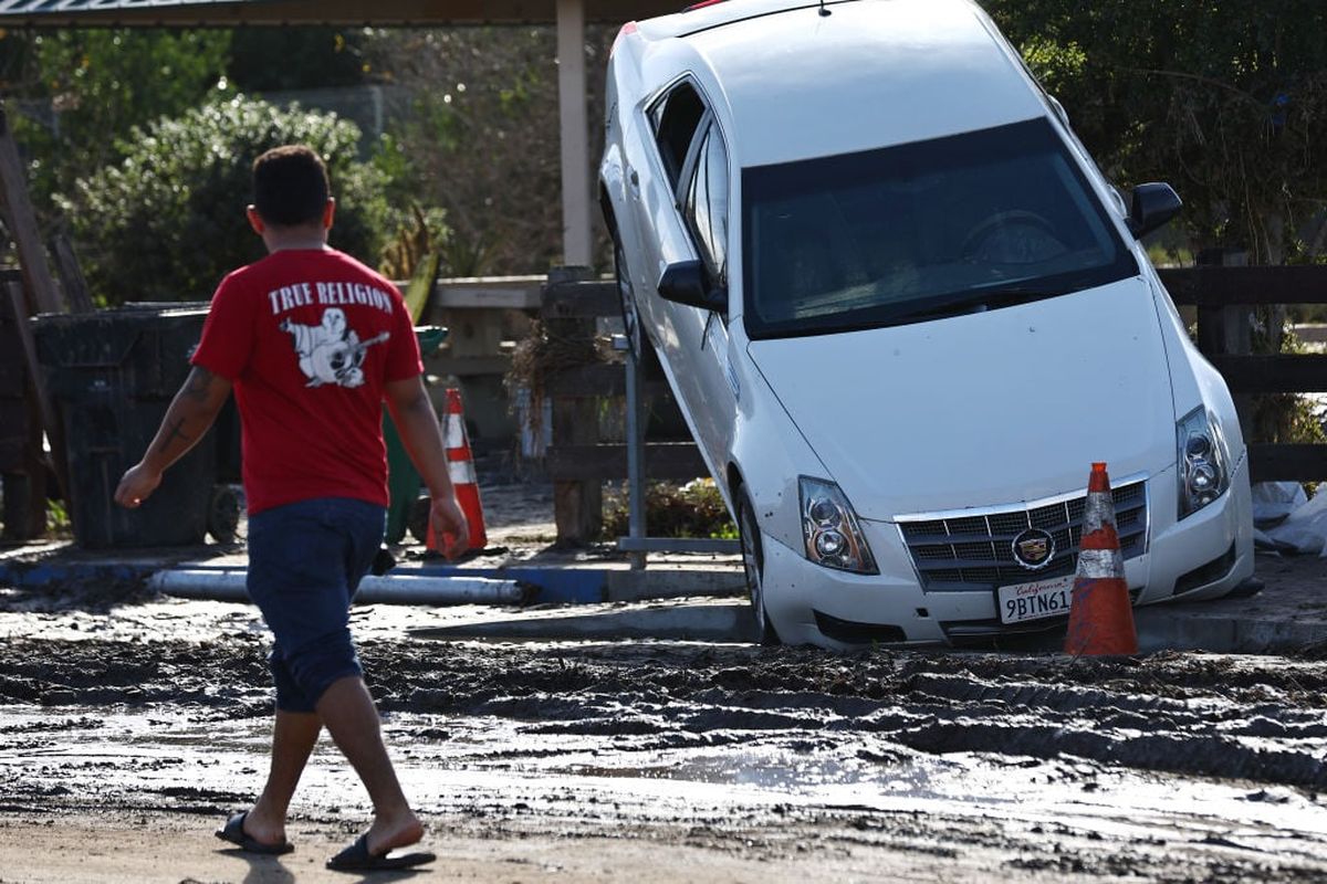 A person stands near a vehicle moved by flooding that remains lodged on a fence the day after an explosive rainstorm deluged areas of San Diego County on Jan. 23 in San Diego, Calif.  (Mario Tama)