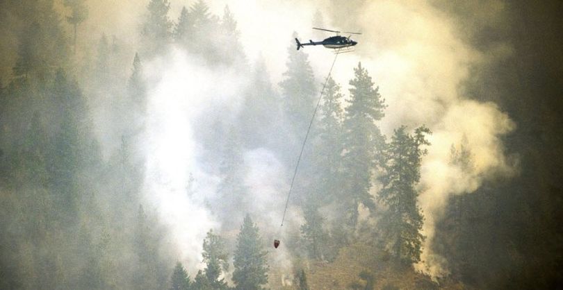 A helicopter carries water to douse the fire that is burning above Bayview, Idaho, Monday, July 6, 2015. The wildfire in northern Idaho has destroyed several homes and forced about hundreds of residents in an upscale lakeside community to evacuate as it ballooned to more than 3 square miles Monday. (Kathy Plonka)