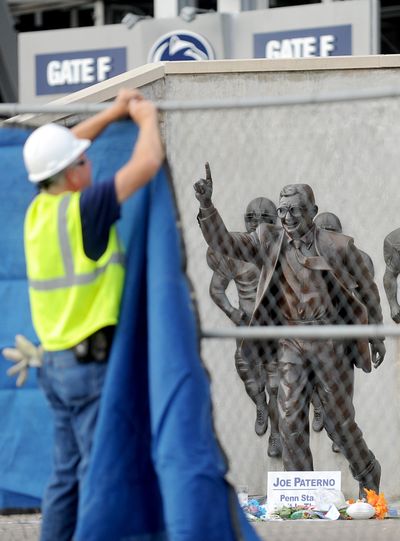 A worker hangs a blue tarp over the fence around the Joe Paterno statue as crews worked to remove it. (Associated Press)