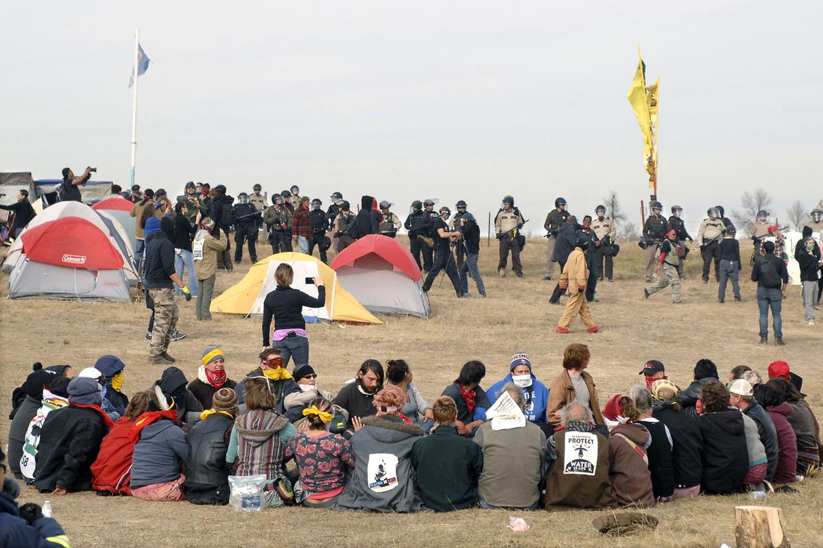 FILE – In this Oct. 27, 2016 file photo, Dakota Access Pipeline protesters sit in a prayer circle at the Front Line Camp as a line of law enforcement officers make their way across the camp to remove the protesters and relocate to the overflow camp a few miles to the south in Morton County, North Dakota. Members of more than 200 tribes from across North America have come to the Standing Rock Sioux Tribe’s encampment at the confluence of the Missouri and Cannonball rivers since August, the tribe says. (Mike McCleary / The Bismarck Tribune via AP)