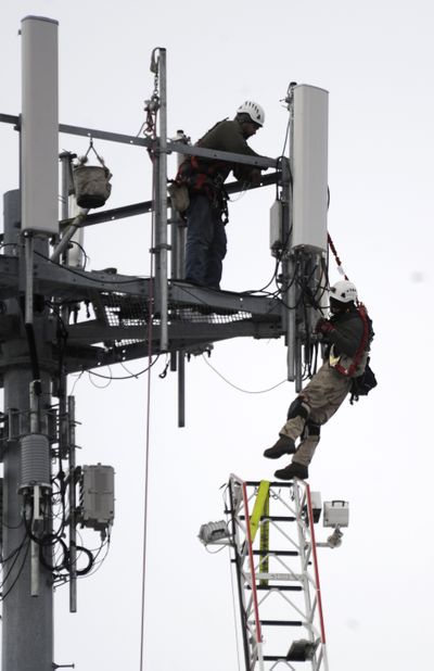 A cell tower worker, right, balances on the end of a fire department ladder Saturday afternoon after he slipped off the tower platform and his fellow worker, left, held on to part of the safety rigging as  the man dangled until the fire department could put up the ladder.  Fire department officials said that the man, who didn't give his name or speak to the media, wasn't securely in his safety harness and was unable to climb back to the platform, even with help from a co-worker.  A technical rescue firefighter climbed the ladder and brought the man down safely. (Jesse Tinsley / The Spokesman-Review)