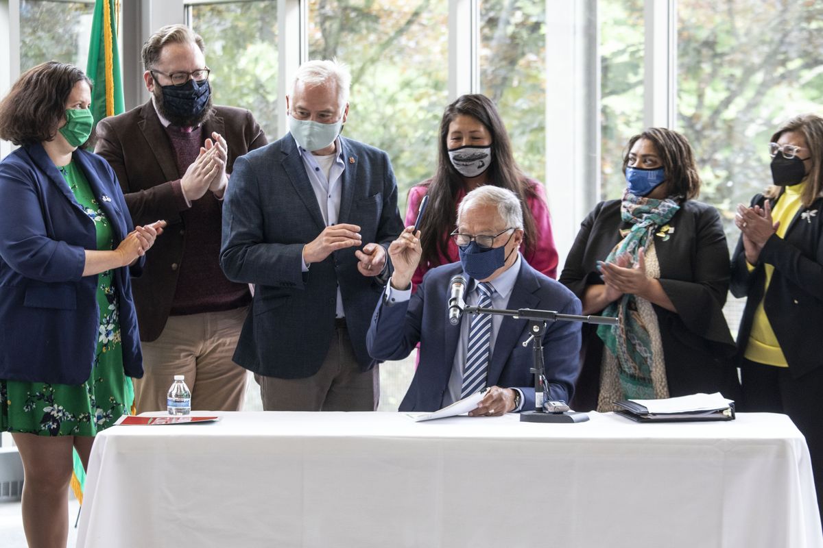 Gov. Jay Inslee signs the first bill, SB 1050 of the Climate priorities package, HB 1050, SB 5126 and HB 1091 at Shoreline Community College, Monday, May 17, 2021, with supporters surrounding him. Inslee will travel to Glasgow next week to attend the United Nations Climate Conference.  (Steve Ringman/Seattle Times)