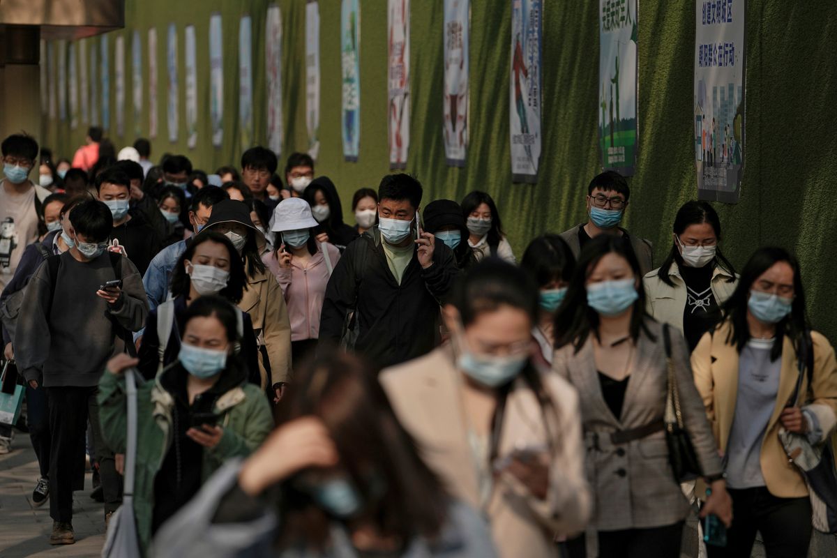 People wearing face masks to help protect from the coronavirus walk by a wall displaying propaganda posters as they head to work at the Central Business District during the morning rush hour, Monday, April 18, 2022, in Beijing.  (Andy Wong)