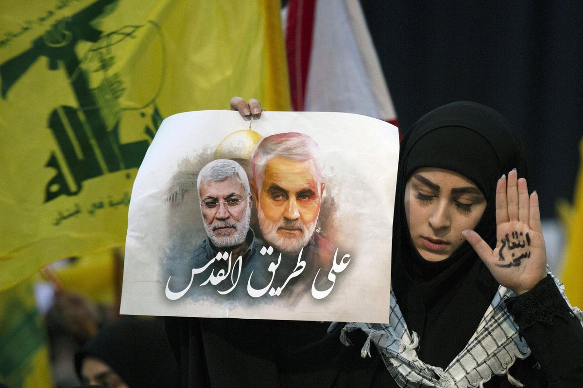 A supporter of Hezbollah leader Sayyed Hassan Nasrallah wears the words “powerful revenge” on her hand, ahead of the leader’s televised speech in a southern suburb of Beirut, Lebanon, Sunday, Jan. 5, 2020 following the U.S. airstrike in Iraq that killed Iranian Revolutionary Guard Gen. Qassem Soleimani. The placard in her other hand depicts Soleimaini and Iraq’s Popular Mobilization forces commander Abu Mahdi al-Muhandis, who was also killed in the strike. Arabic on placard reads: “On the road to Jerusalem.” (Maya Alleruzzo / Associated Press)