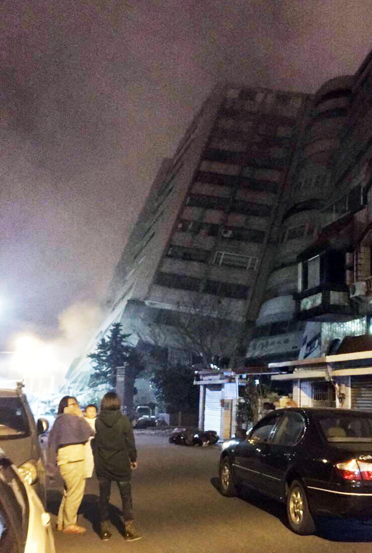 In this photo released by Hualien County Fire Bureau, Taiwanese people watching a building that collapsed on its side from an early morning earthquake in Hualien County, eastern Taiwan, early Wednesday, Feb. 7 2018. A 6.4-magnitude earthquake has struck eastern Taiwan, according to the U.S. Geological Survey. (Hualien County Fire Bureau / AP)
