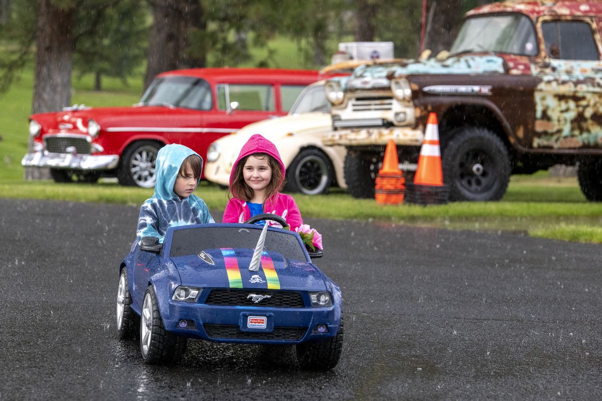Avery Puckett, 5, left, rides shotgun while Lillian Green, 8, pilots her unicorn-themed electric car around the planned car show in the pouring rain at Greenwood Memorial Terrace on Sunday. The cemetery planned a Memorial Day event with a car show, free hot dogs and live music but heavy rain dampened the event.  (Jesse Tinsley/THE SPOKESMAN-REVIEW)