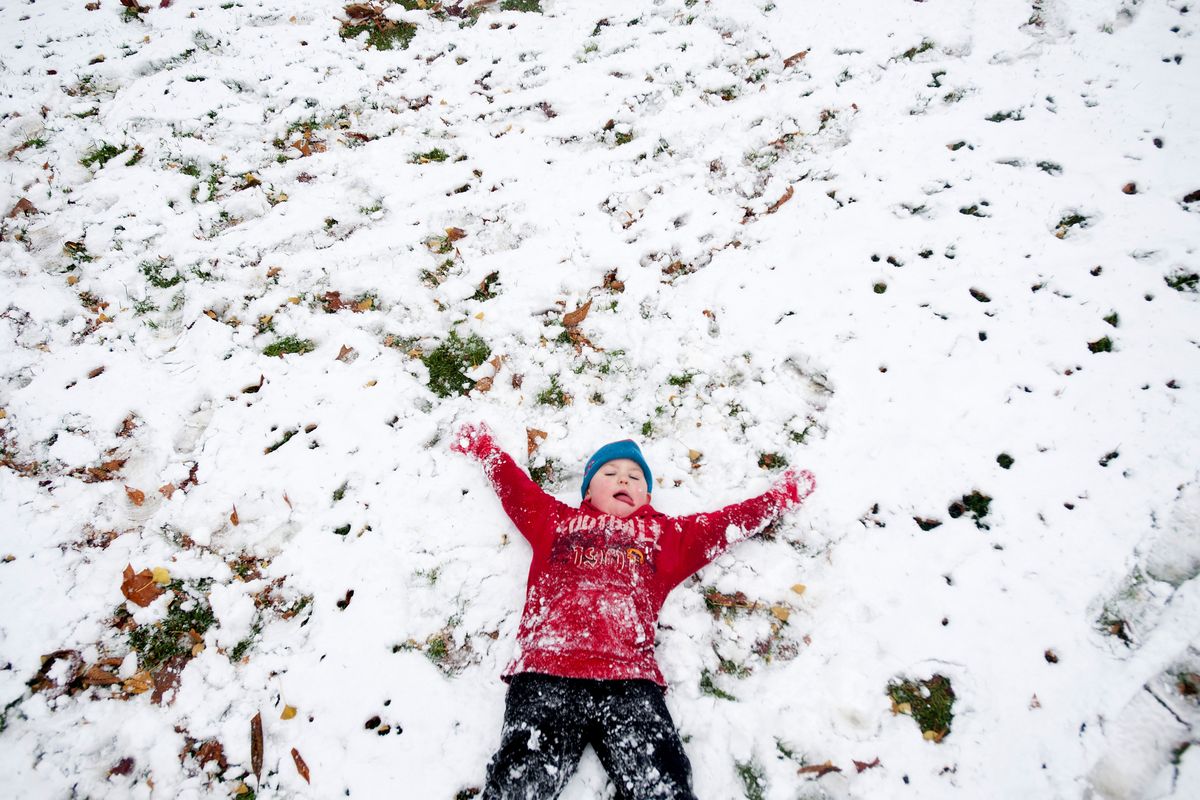 Miky Murinko, 4, of Spokane, makes a snow angel as he plays in the first snowfall of the year with his mother, Rion, on Friday at Coeur d