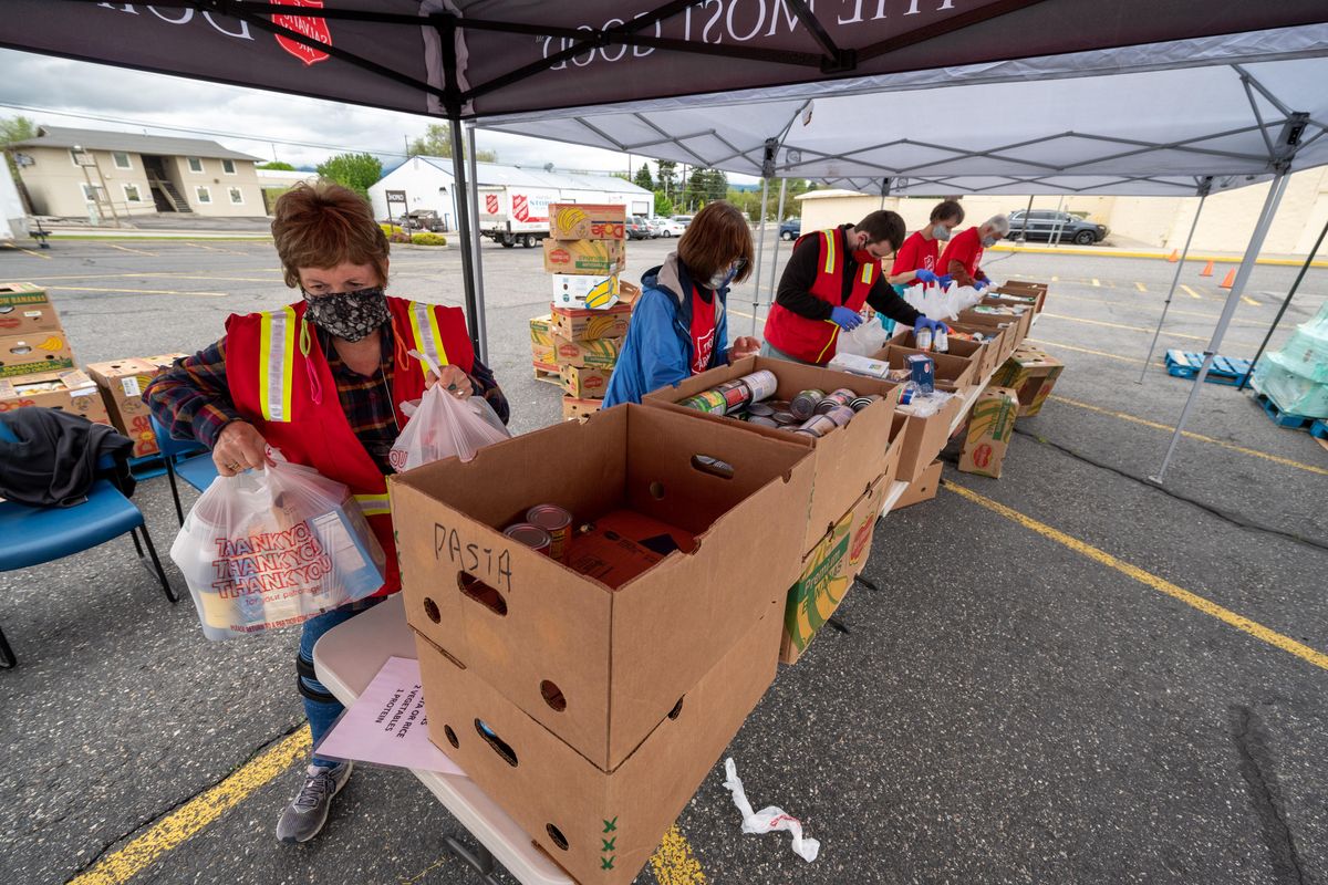 Karen Seyfert, on far left, and other Salvation Army volunteers, bag up cans of food, Tues., May 19, 2020. The Salvation Army of Spokane distributed over 600 food boxes for local families in need. This is part of a mass distribution of food by The Salvation Army throughout Washington state. In the Spokane Valley, a drive-through food distribution fed a steady stream of hundreds of car lined in the parking lot of the Opportunity Shopping Center. Funding for the food boxes was provided by The Church of Jesus Christ of Latter-day Saints. (Colin Mulvany / The Spokesman-Review)