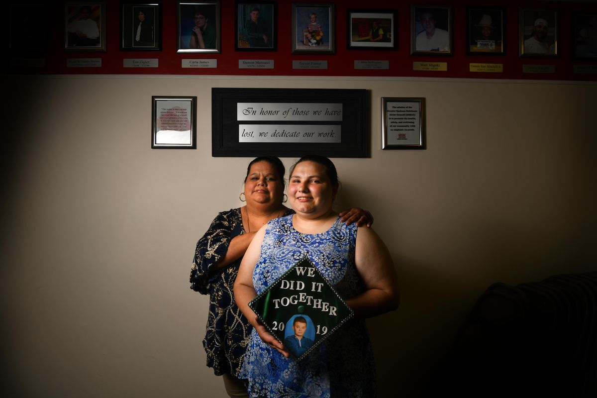 Christine Dugger, right poses for a photo with her mother, Amanda Dugger, while holding her East Valley High School graduation cap adorned with a photo of her best friend Brandon Dunkle, who died in front of her after being hit by a drunk driver in 2016 on Wednesday, June 19, 2019, at Greater Spokane Substance Abuse Council