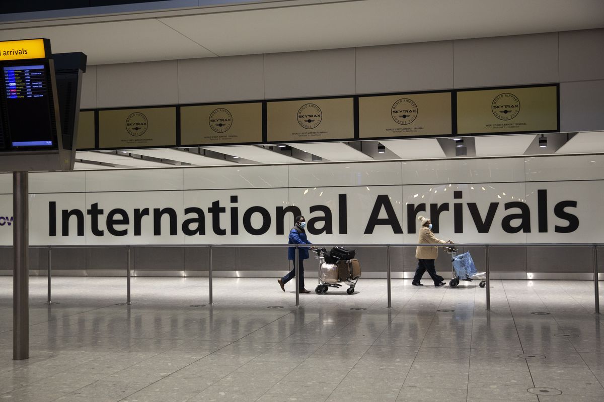 FILE - In this Tuesday, Jan. 26, 2021 file photo, arriving passengers walk past a sign in the arrivals area at Heathrow Airport in London, during England