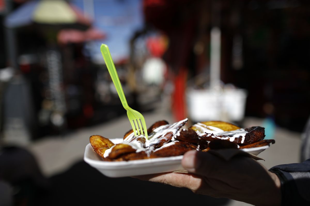 A customer receives his order of fried plantains, served on a non-biodegradable disposable plate along with a plastic fork, from a street vendor in central Mexico City, Friday, Jan. 1, 2021. The few street food vendors out working on New Year