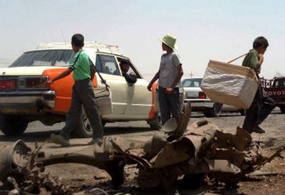 
Iraqi boys sell drinks to commuters behind the remains of a car after a bombing Tuesday in Kirkuk, Iraq.
 (Associated Press / The Spokesman-Review)