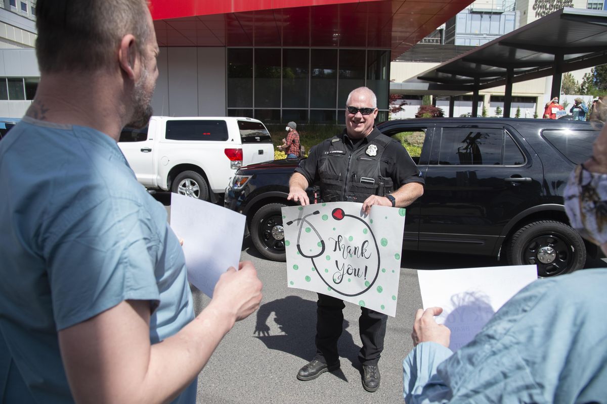 Spokane Police Officer Jim Christensen stops his car and holds a sign expressing his thanks to the staff of Providence Sacred Heart Medical Center who lined up along 8th Avenue through the hospital campus Tuesday, April 28, 2020 at noon to return the sentiment with signs of their own in Spokane, Washington. An array of police, fire department vehicles and ambulances paraded past Providence Sacred Heart, Multicare Deaconess, Holy Family and the Veterans Administration hospitals to thank the medical personnel for their work against the COVID-19 virus. (Jesse Tinsley / The Spokesman-Review)