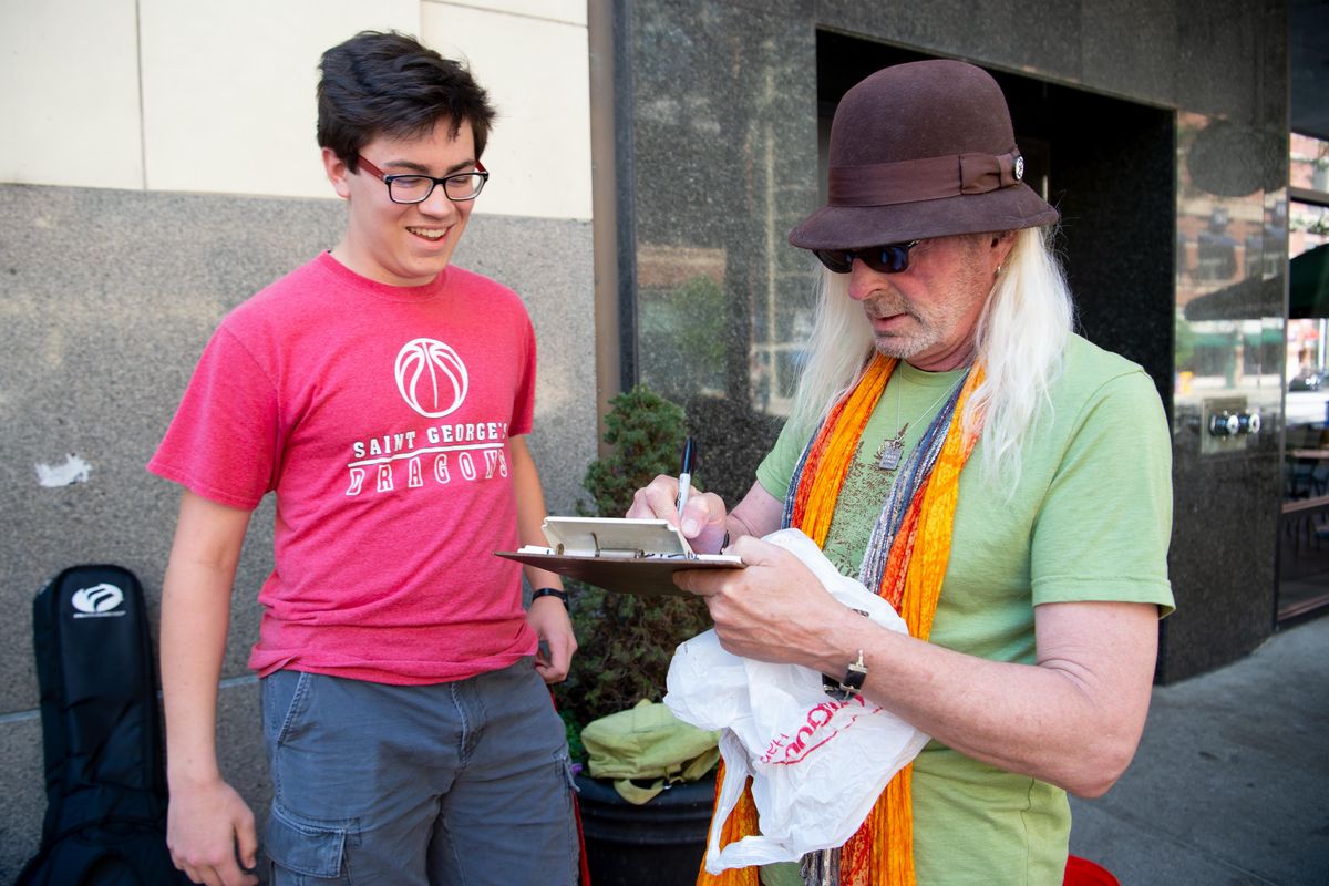 Ben Clark, left, signs up with organizer Jim Lyons to play at Street Music Week in downtown Spokane Thursday, June 13, 2019. It was the first participation in Street Music Week for the Clark and a group of students from St. George’s School in north Spokane. (Jesse Tinsley / The Spokesman-Review)