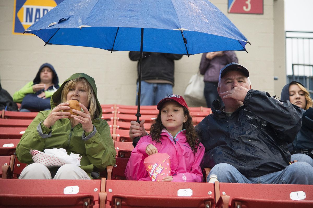 Katy Phillips, Ella Mayer and her dad Doug, eat burgers and snacks while waiting out a rain delay on Spokane Indians opening night, Thursday, June 15, 2017. (Colin Mulvany / The Spokesman-Review)