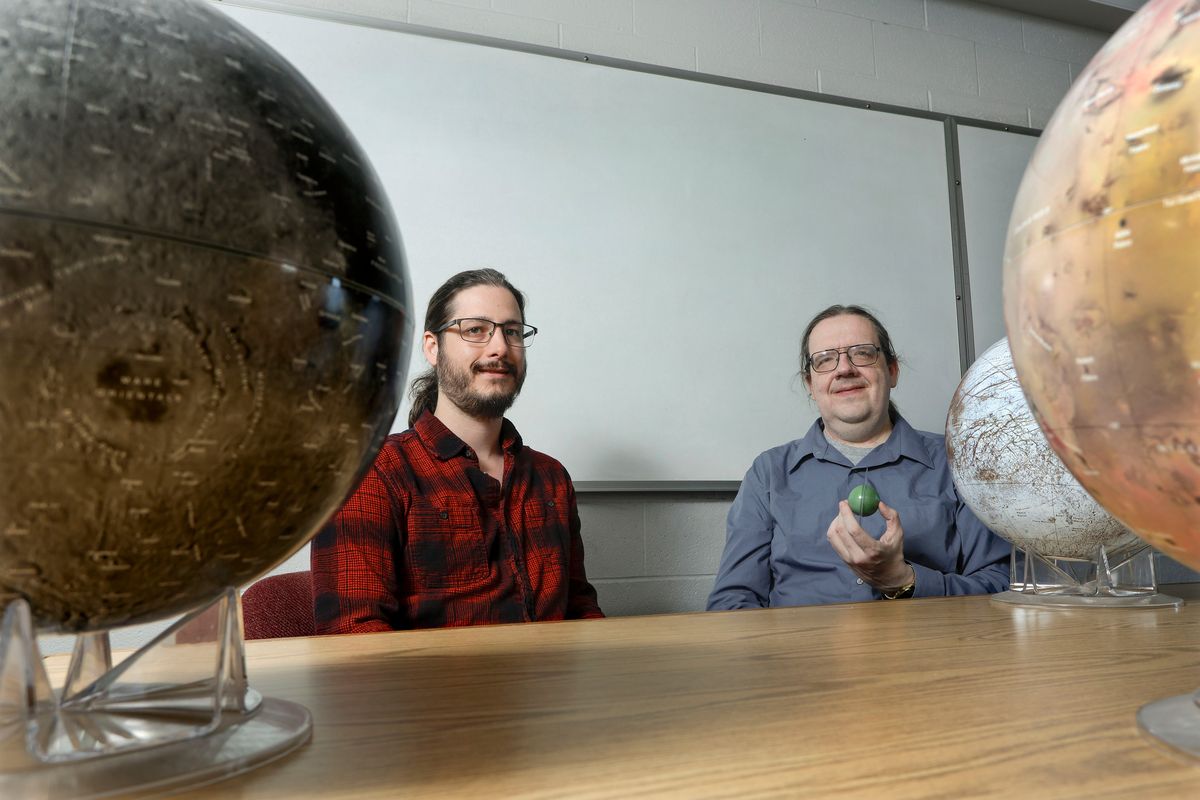 University of Idaho graduate student Jacob Herman, left, and professor Matthew Hedman are seen with models of moons from our solar system on Tuesday in Moscow, Idaho. Hedman and Herman analyzed images from the James Webb Space Telescope as part of a team that discovered a new moon of Uranus.  (Geoff Crimmins/For The Spokesman-Review)