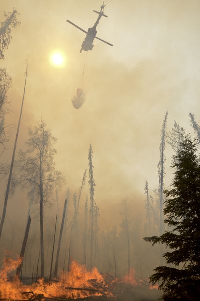 A helicopter dumps water on a portion of the Funny River fire, Sunday in the Funny River community in Soldotna, Alaska. (Associated Press)