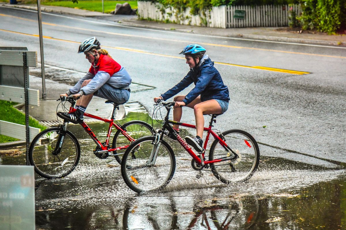 Summer Parkway cyclists raise their feet as they splash through a puddle at the corner of Manito Boulevard and 29th Avenue, Thursday, June 21, 2018, in Spokane, Wash. (Dan Pelle / The Spokesman-Review)