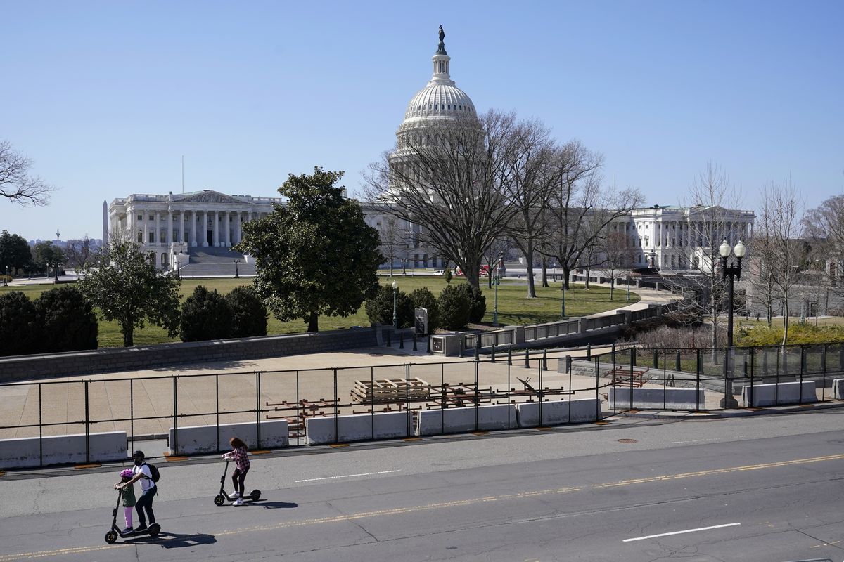 People ride scooters past an inner perimeter of security fencing on Capitol Hill in Washington, Sunday, March 21, 2021, after portions of an outer perimeter of fencing were removed overnight to allow public access.  (Patrick Semansky)