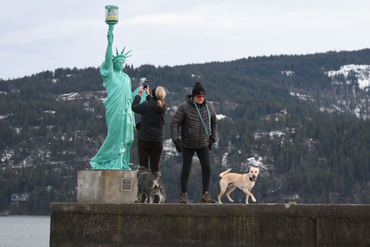 Sandpoint residents Audrey Milch, left, and Lawrence Blakey check out the mini Statue of Liberty at City Beach park on Dec. 19 in Sandpoint with their dogs Callie, a schnauzer, and Goose, a Labrador-Chihuahua mix. “It looks good with this backdrop, doesn’t it?” Milch said. “Stunning.” (James Hanlon/The Spokesman-Review)