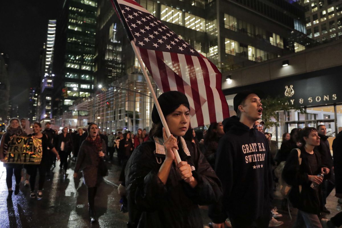 A protester carries an upside down American flag as she walks along Sixth Avenue while demonstrating against President-elect Donald Trump, Wednesday, Nov. 9, 2016, in New York. Thousands of protesters around the country took to the streets Wednesday to condemn the election of Trump as president. (Julie Jacobson / Associated Press)