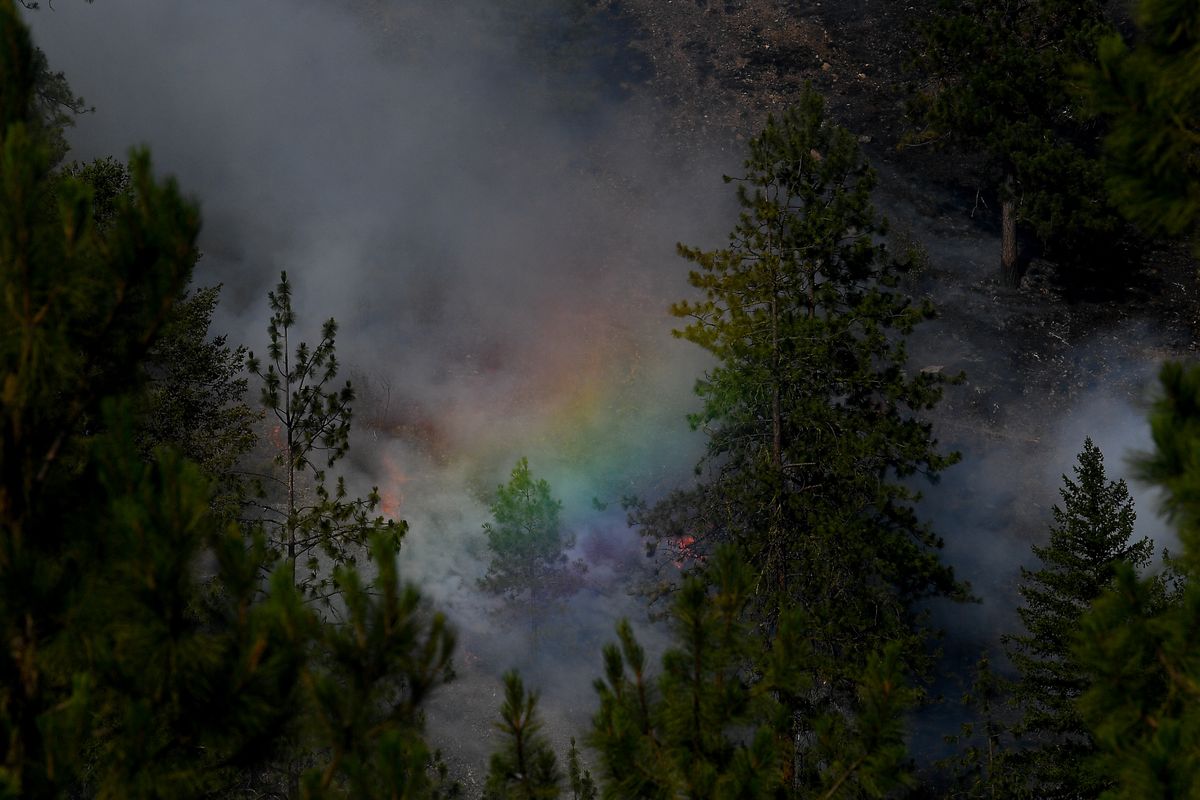 Water dropped from air assets casts a rainbow against a smoldering landscape as crews work to suppress a wildfire on Saturday, July 3, 2021, off Highway 291 southeast of Tum Tum, Wash.  (Tyler Tjomsland/The Spokesman-Review)