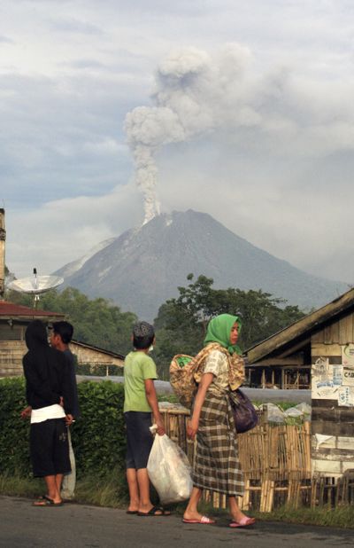 Villagers watch Monday as Mount Sinabung spews smoke and ash in Tanah Karo,  Indonesia. The volcano that had been dormant for more than 400 years erupted for the second day in a row Monday, forcing the evacuation of 30,000 people.  (Associated Press)