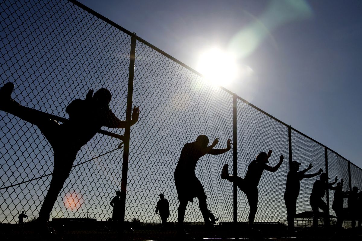 It’s tuneup time in Peoria and Mariners players use a fence to get in some stretching during the opening day of spring training Monday. (Associated Press)