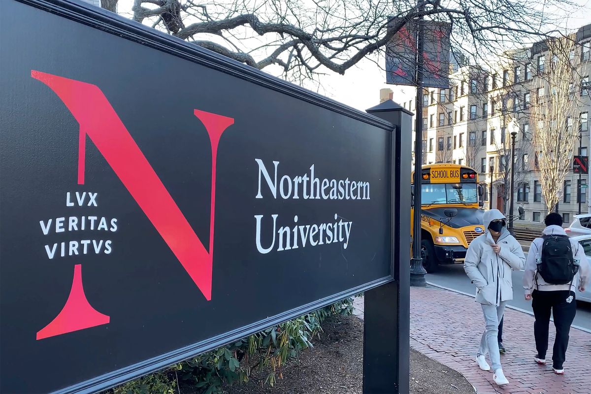 Pedestrians walk near a Northeastern University sign on the school's campus in Boston, Jan. 31, 2019. At Northeastern University in Boston, one of a growing number of schools requiring boosters, students are returning to campus as planned.  (Rodrique Ngowi)