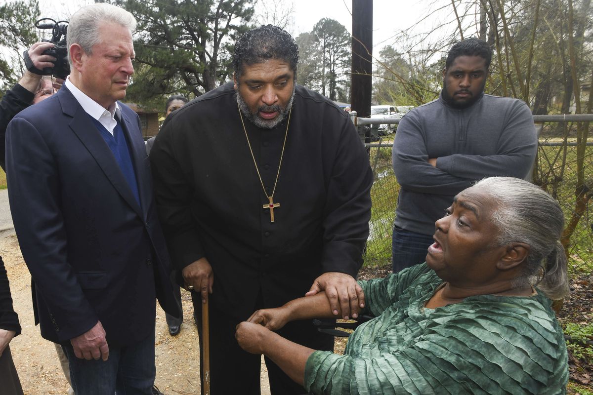 FILE - In this Feb. 21, 2019, file photo, former Vice President Al Gore, left, founder of the Climate Reality Project, and the Rev. William Barber II, president of the Repairers of the Breach, visit Lowndes County resident Charlie Mae Holcombe to talk about the failing wastewater sanitation system at her home in Hayneville, Ala. An anti-poverty coalition led by Barber is scheduled to hold a virtual march Saturday. The Mass Poor People’s Assembly & Moral March on Washington aims to build upon the nation’s principles to pursue solutions to poverty — something advocates say is getting especially severe in rural areas.  (Julie Bennett)